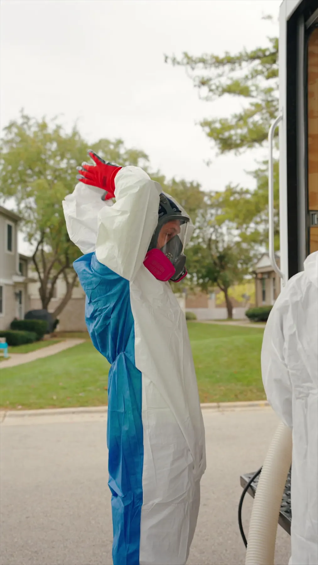 Building Energy Experts worker in protective equipment beside a work trailer at a multifamily property